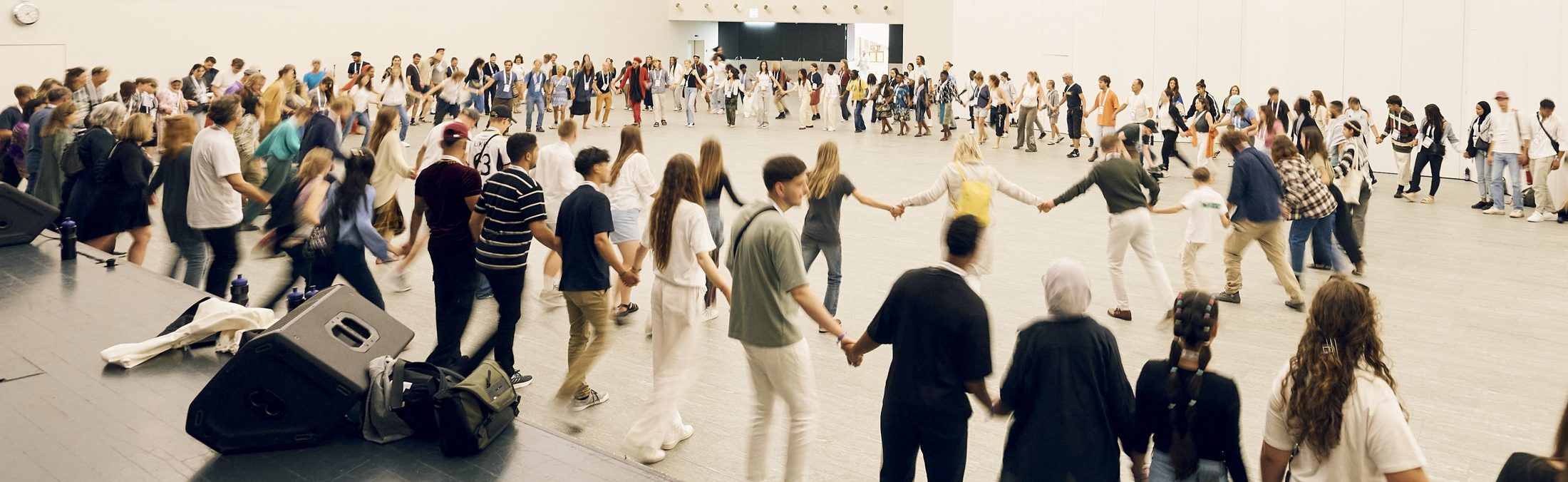 A large circle of people holding hands in a bright hall